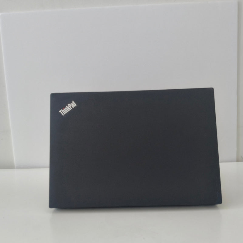 Black lenovo thinkpad laptop on a white surface with a white wall background